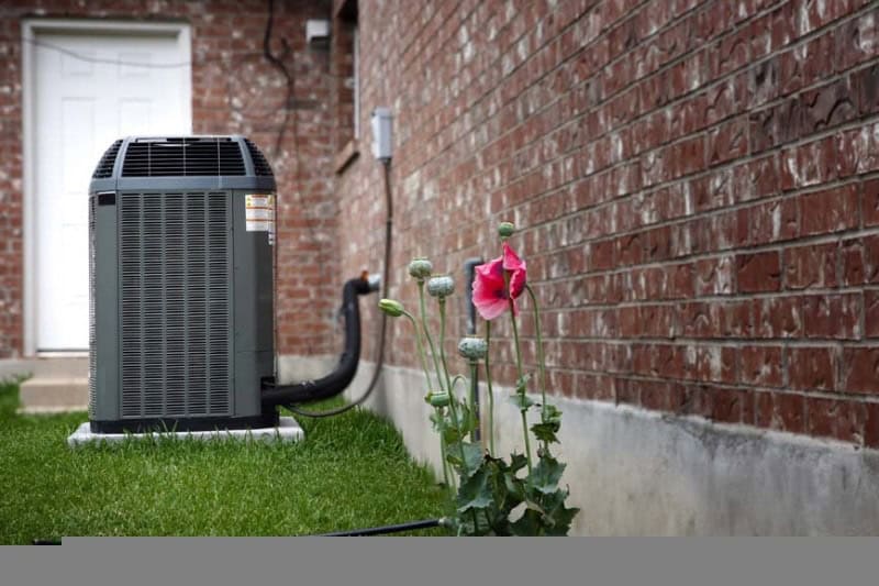 Air conditioning unit outside next to a pink flower