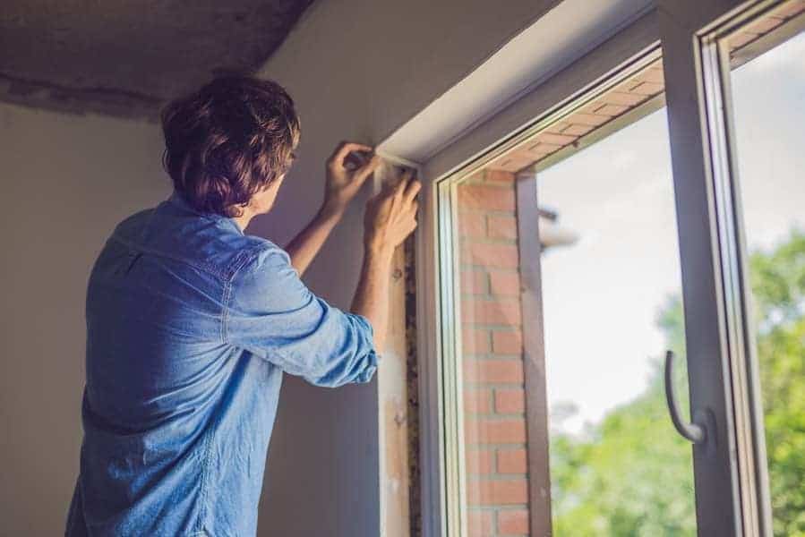 Man checking window insulation as part of the heat gain prevention tips.