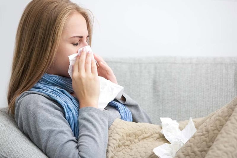 Does an AC Help With Allergies? Close up of a young woman sneezing into a tissue.