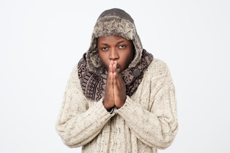 man trying to stay warm and figure out why his home's heat pump is blowing cold air