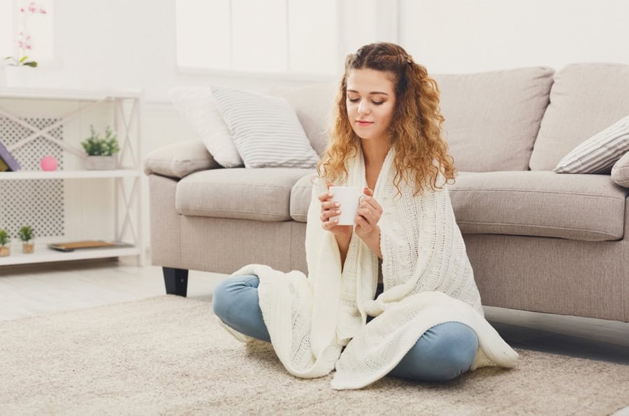 Woman staying comfy indoors with cup of coffee after learning how she can make her furnace last longer.