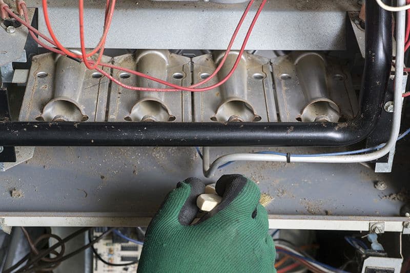 Someone working on a furnace with green gloves. 5 Reasons to Schedule a Fall Furnace Clean and Check.