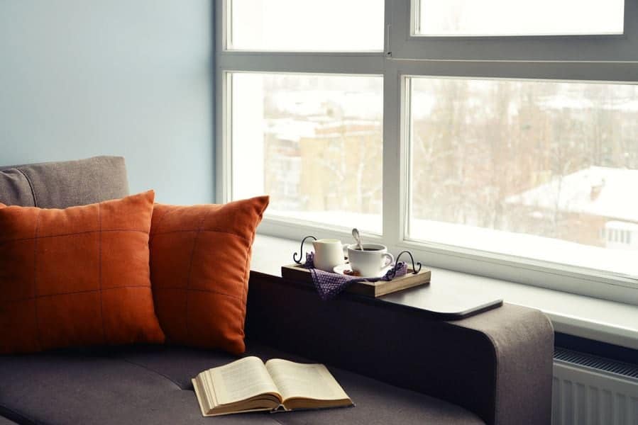 Image of a couch with a book and drinks on it. How to Lower Your Winter Heating Bill.