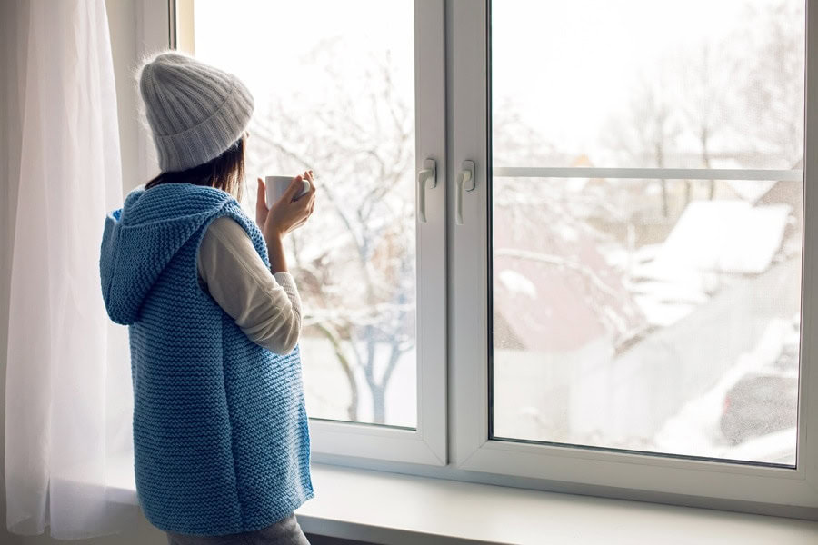 Woman looking out the window in the winter after determining how she can save money on her heating bill.