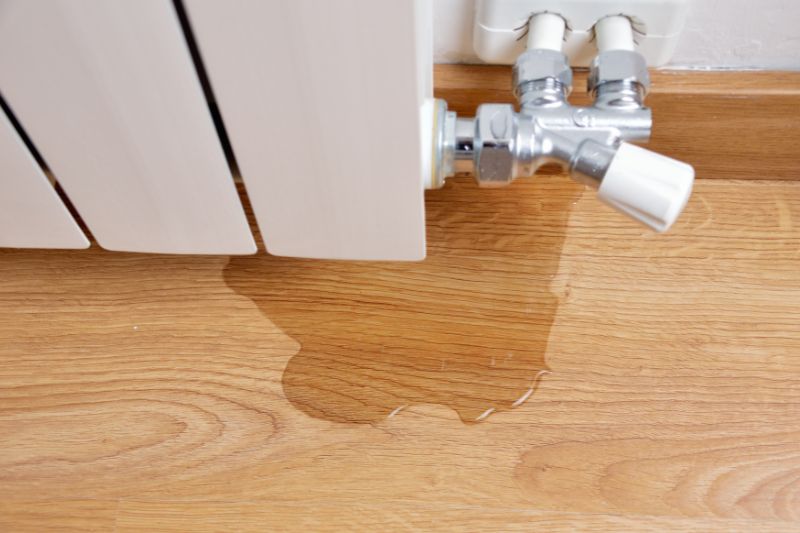 Radiator with a valve leaking water onto a wooden floor.