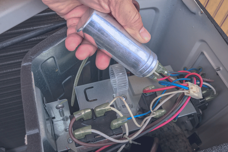 Close-up of a hand holding a metal tool near an electrical control box with multiple colored wires and terminals, indicating wiring work on a appliance component.